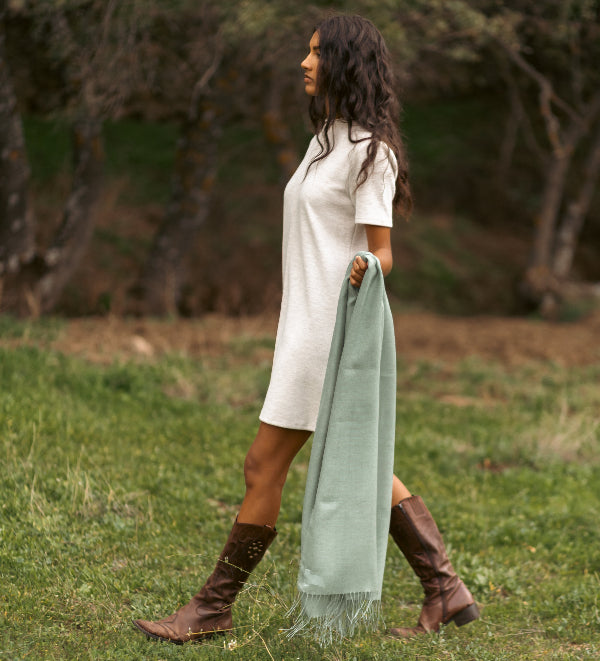 Modelo femenina en un entorno rural llevando un chal liso de baby alpaca y seda color frost green