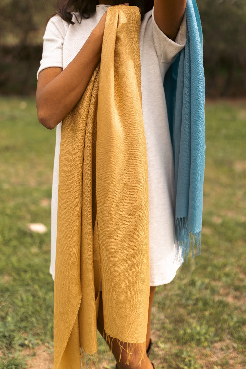 Modelo femenina en un entorno rural con un chal de baby alpaca y seda color miel mostaza