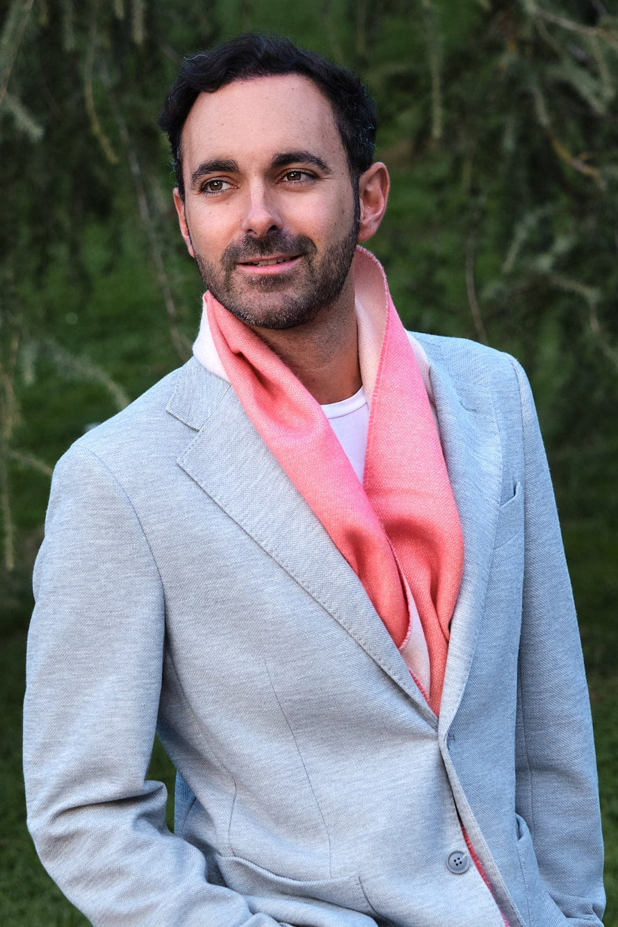 Hombre en un jardín con bufanda de baby alpaca de color coral y blanco