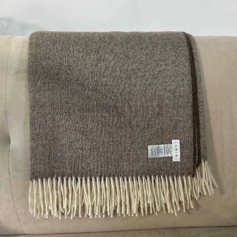 Manta de lana de baby alpaca de color blanco y tabco soblada sobre un sofá de color claro