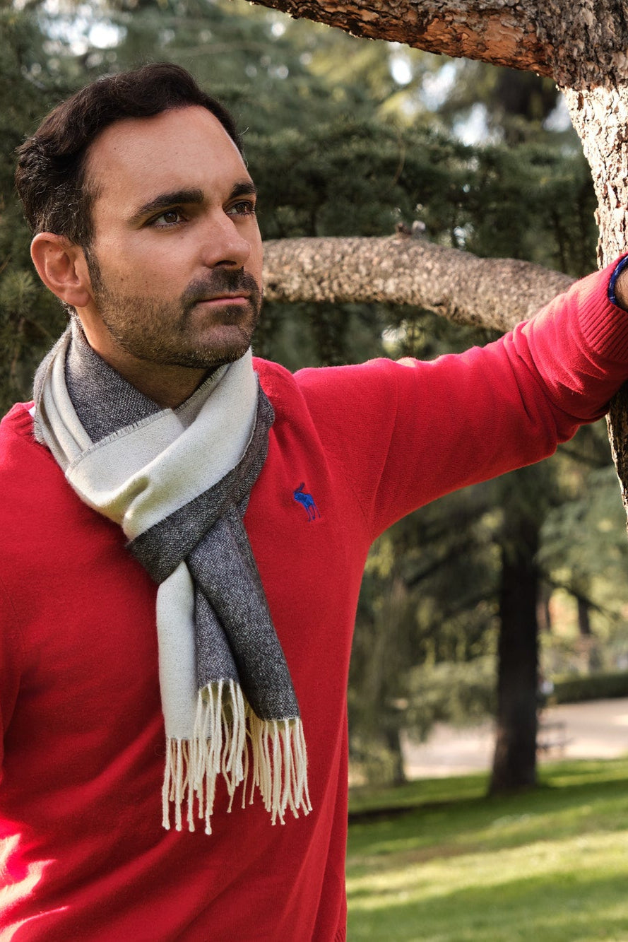 Hombre en el campo apoyado en un árbol con una bufanda de lana de baby alpaca gris y blanca