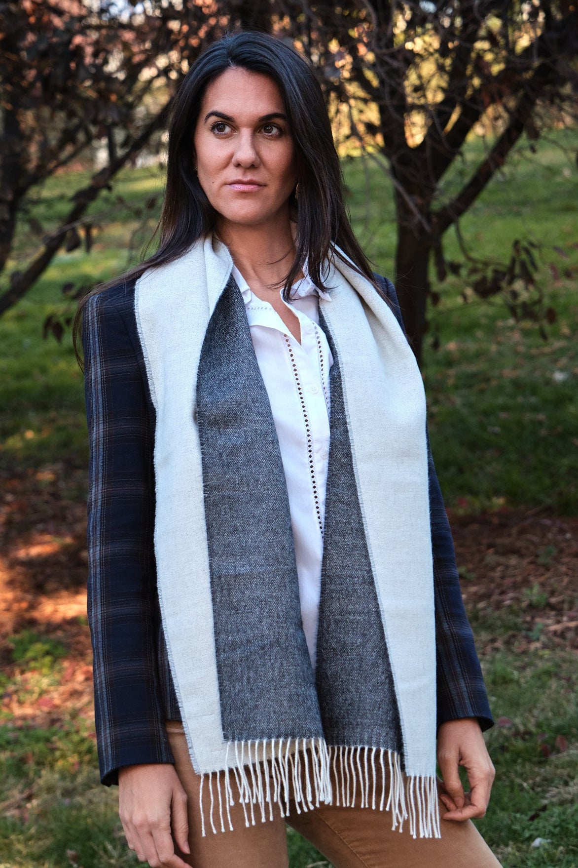 Mujer morena en el campo con una bufanda de lana de baby alpaca de color gris y blanca